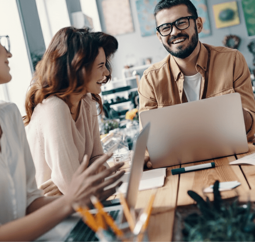 Three people grouping together on a working desk with laptops and notebook laughing