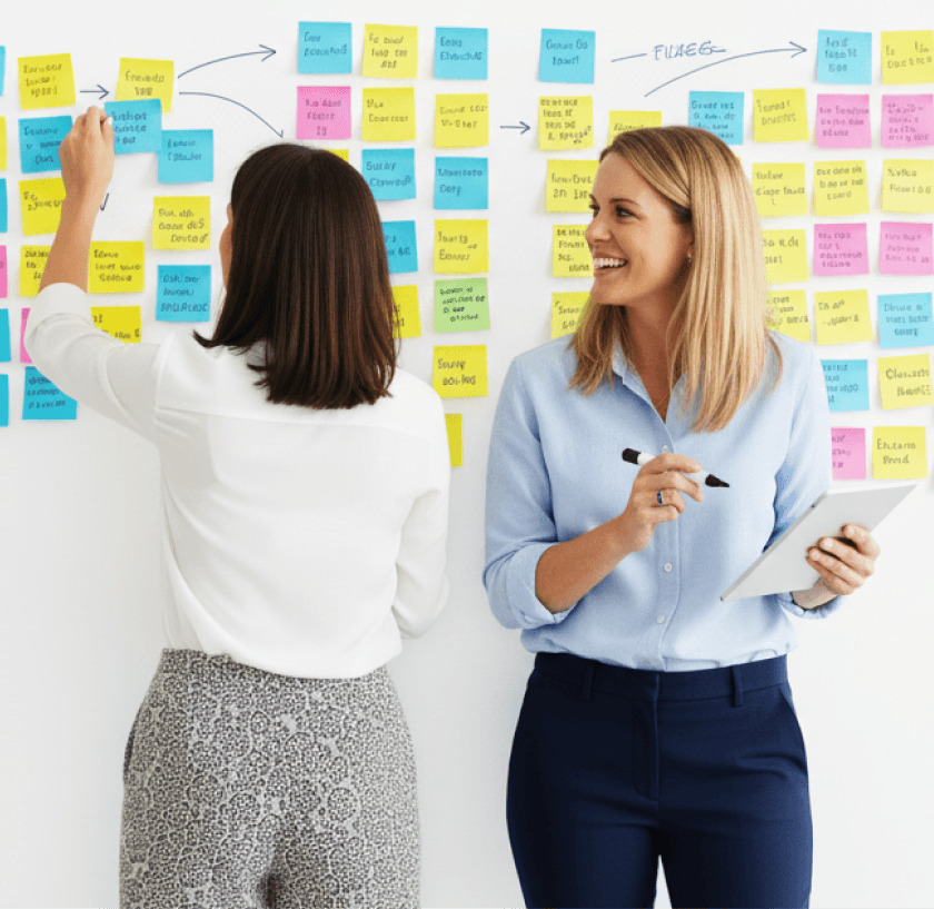 Two ladies sticking sticky notes onto a wall